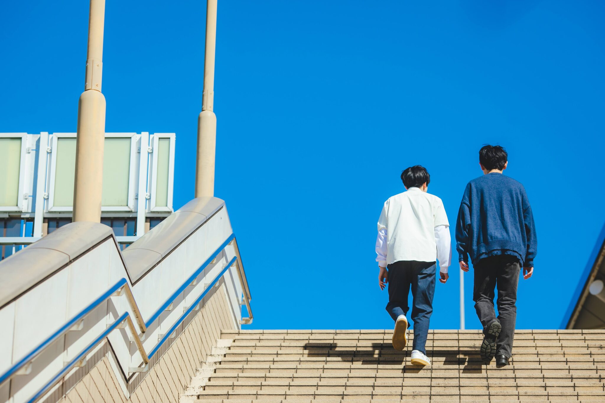 青空の元階段を上る男性二人