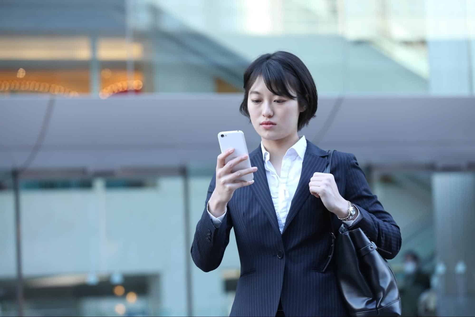 街中でスマホを見るスーツ姿の女性