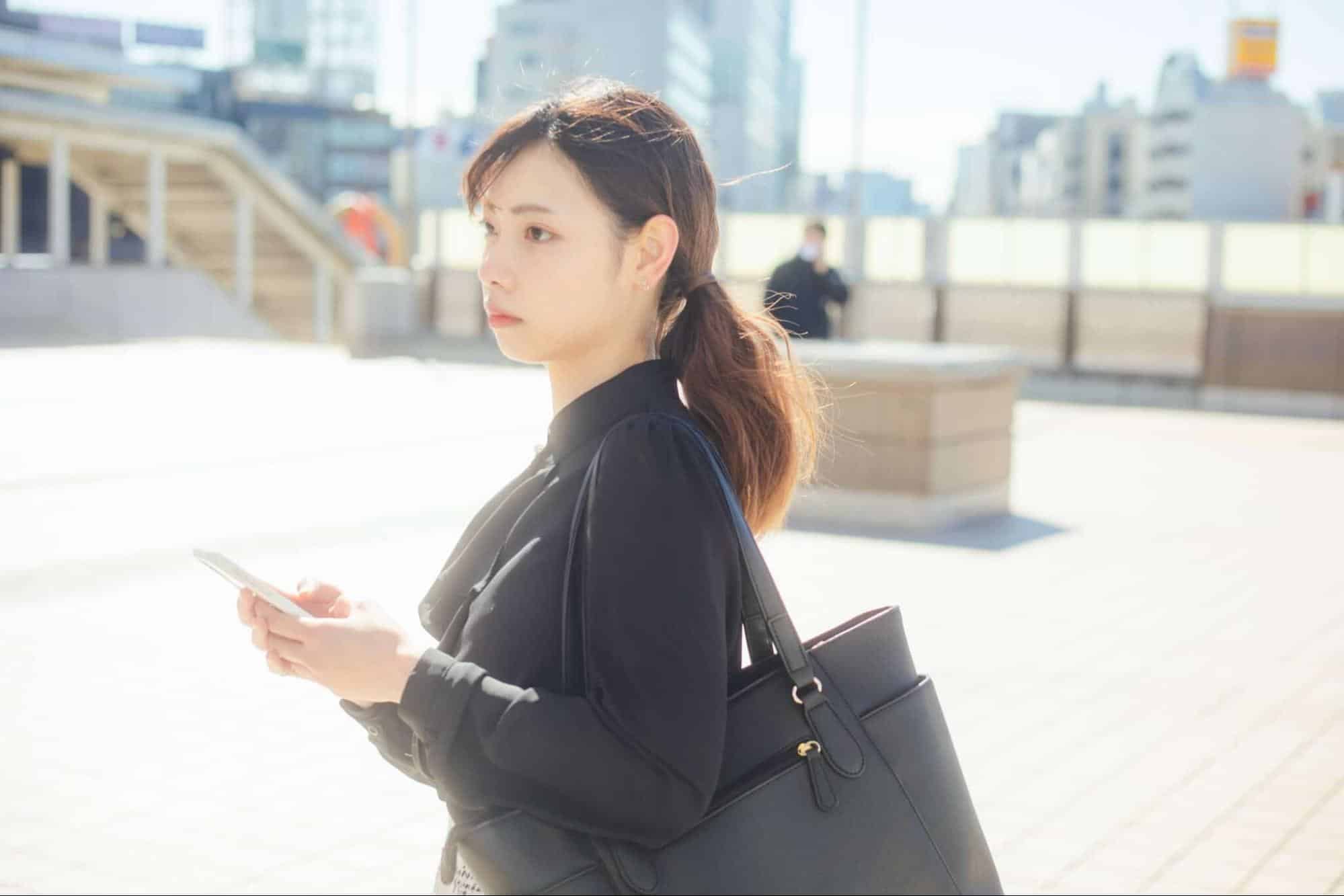 スマホを持ち遠くを眺めるスーツ姿の女性