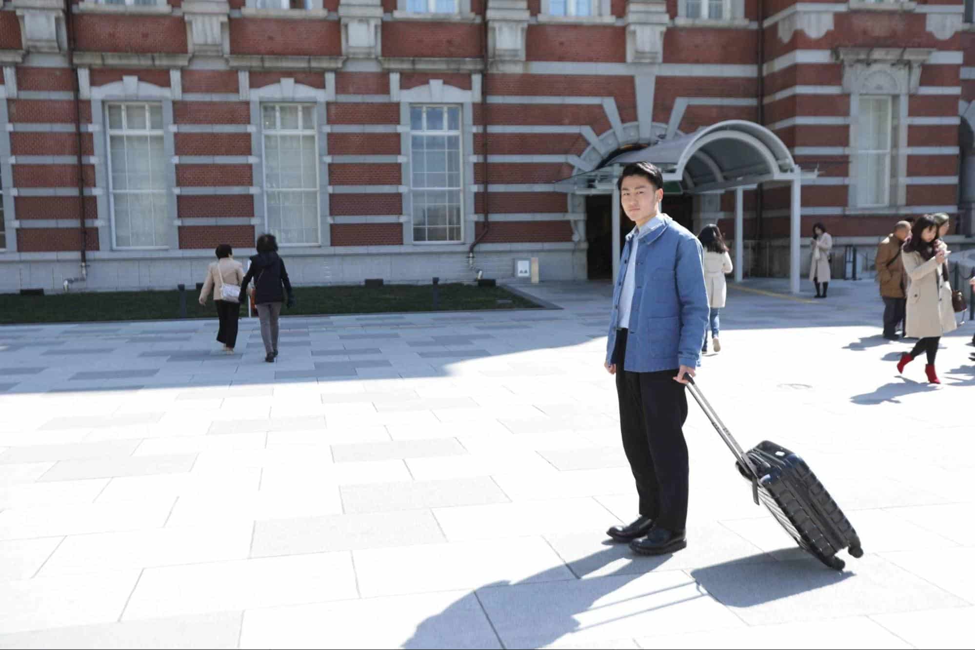 駅の前でキャリーバッグを引く男性